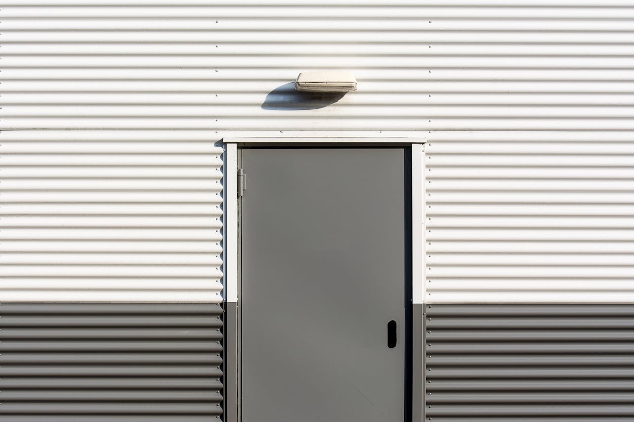 Minimalist image of a corrugated metal wall with a centered door, showcasing industrial architecture.